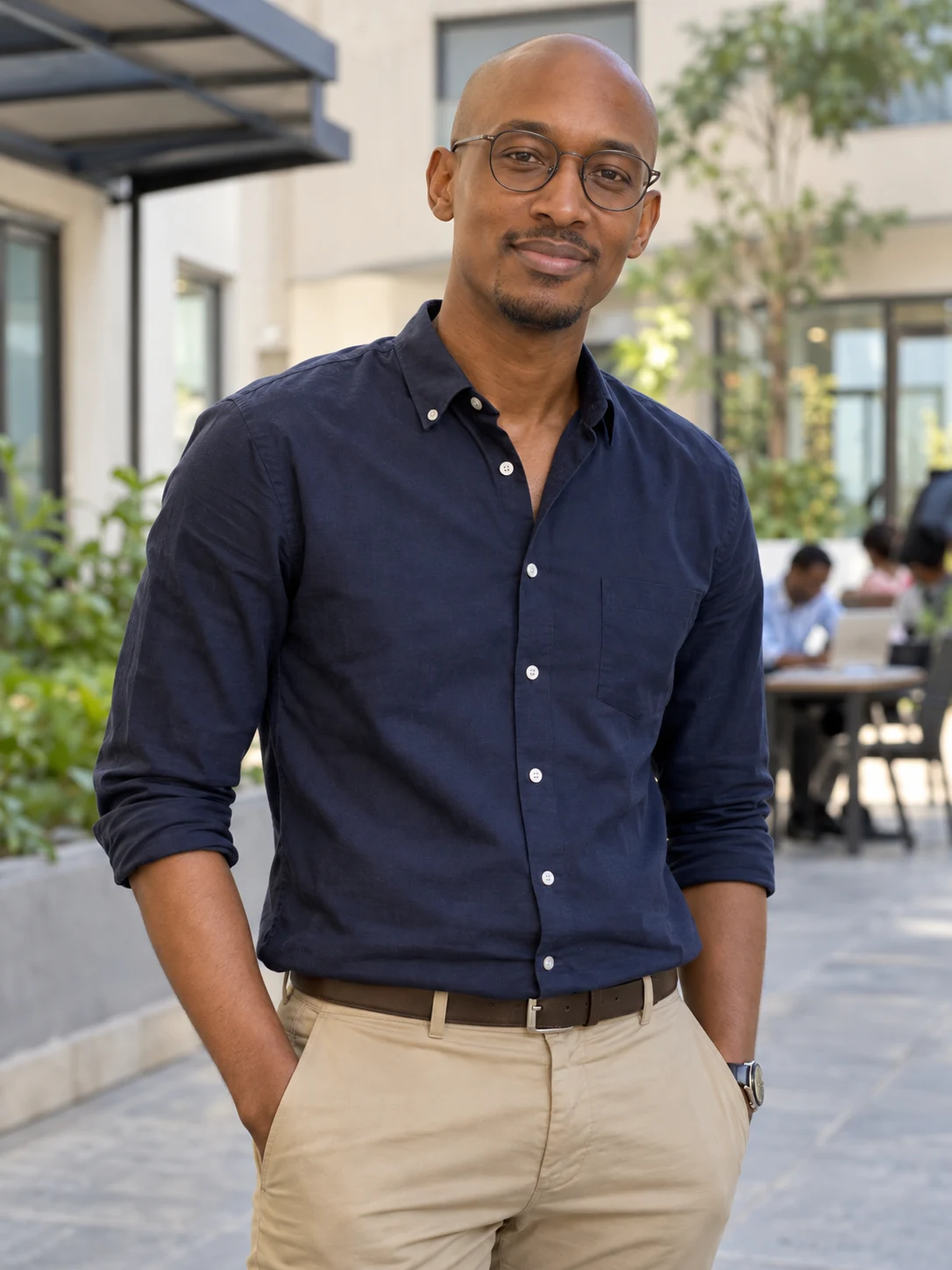 Kunle, a fictional adult AI character, wearing glasses and a navy shirt.